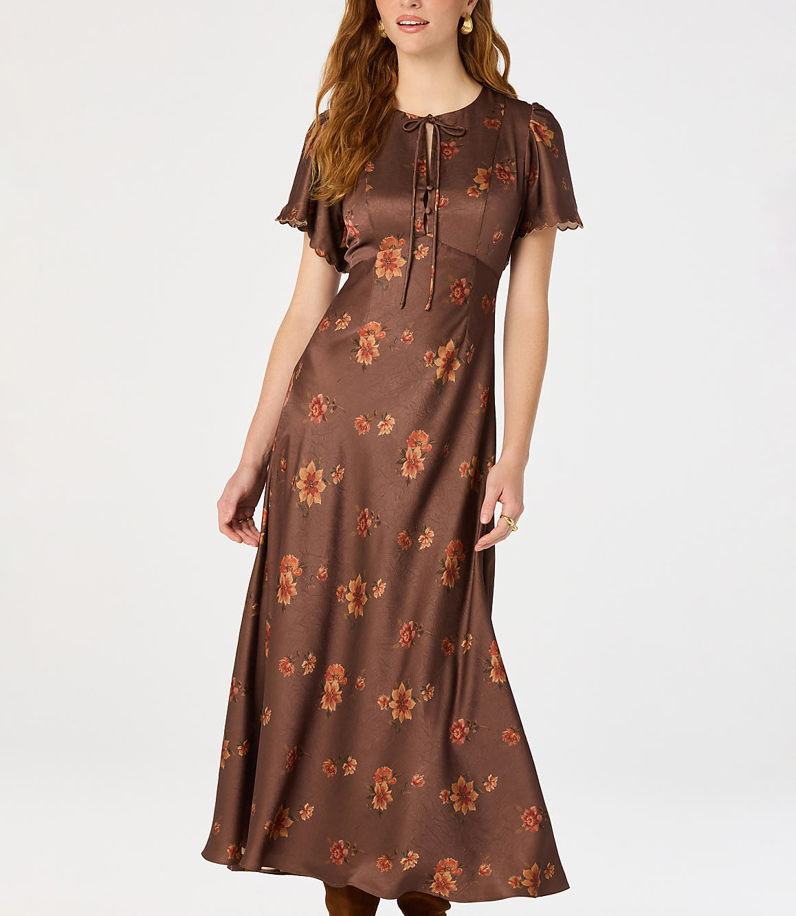 A woman in a brown floral midi dress stands against a plain white background.