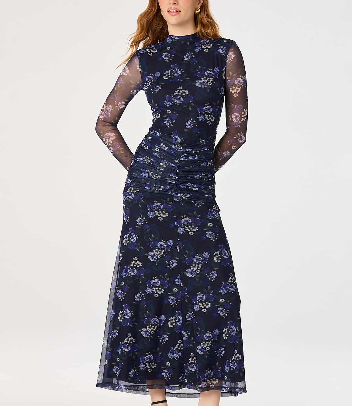 A woman in a dark floral mesh dress stands against a plain white background.