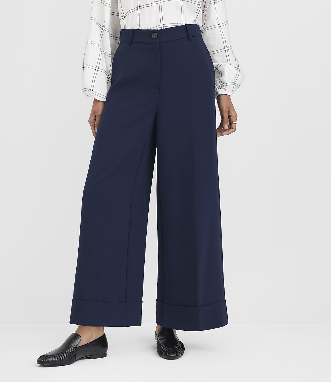 A person in navy wide-leg pants and a checkered blouse stands against a plain white background.