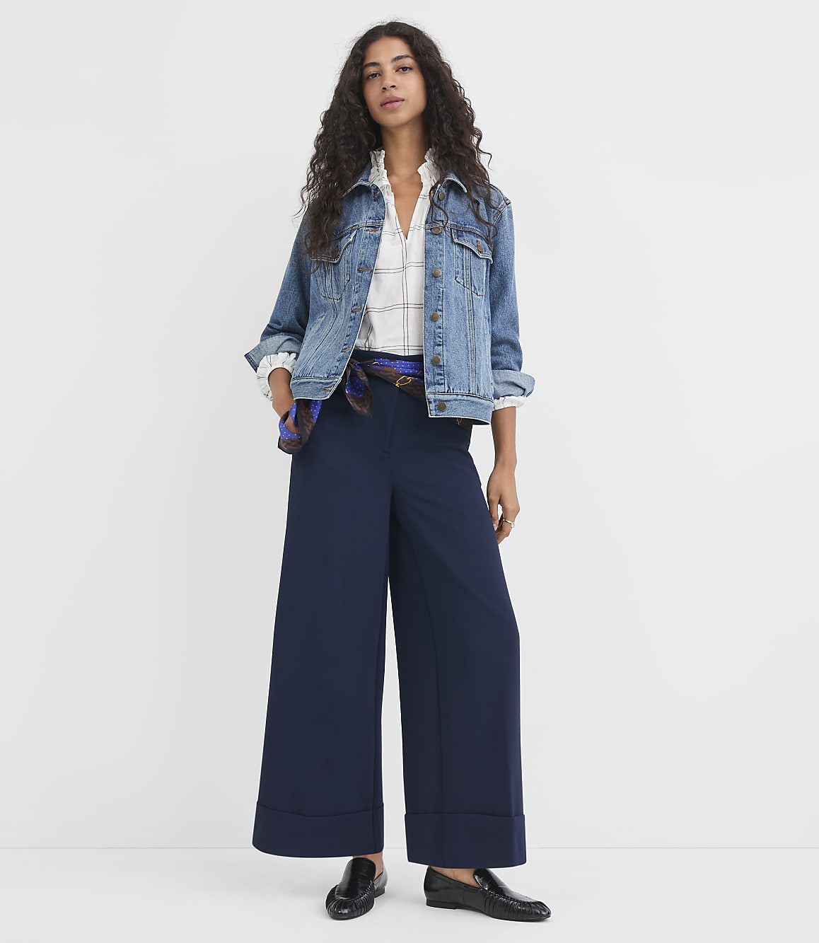 A woman in a denim jacket and wide-leg navy pants stands against a plain white background.