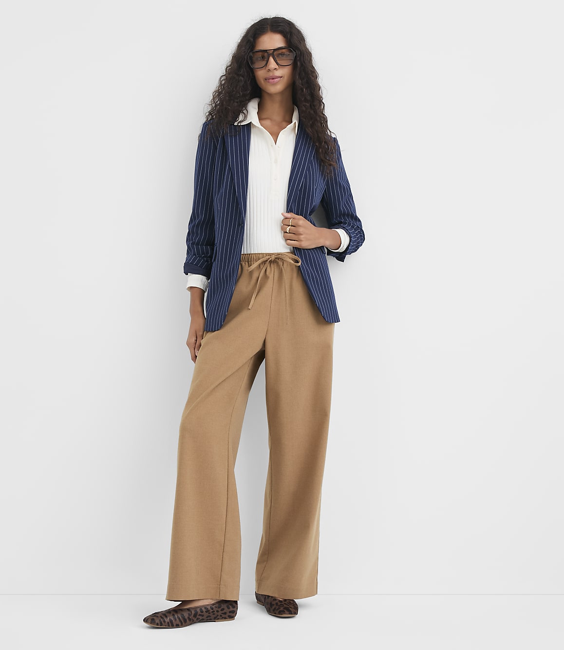 A woman in a striped blazer and wide-leg pants stands against a plain white background.