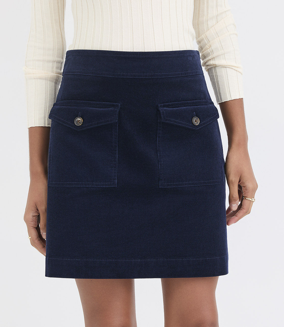 A navy blue corduroy skirt with two front pockets is worn by a person against a plain white background.