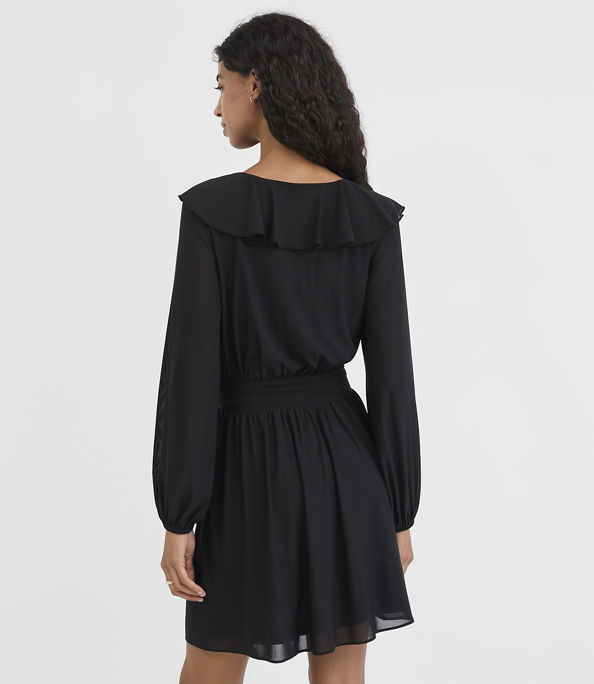A woman in a black ruffled dress stands against a plain white background.