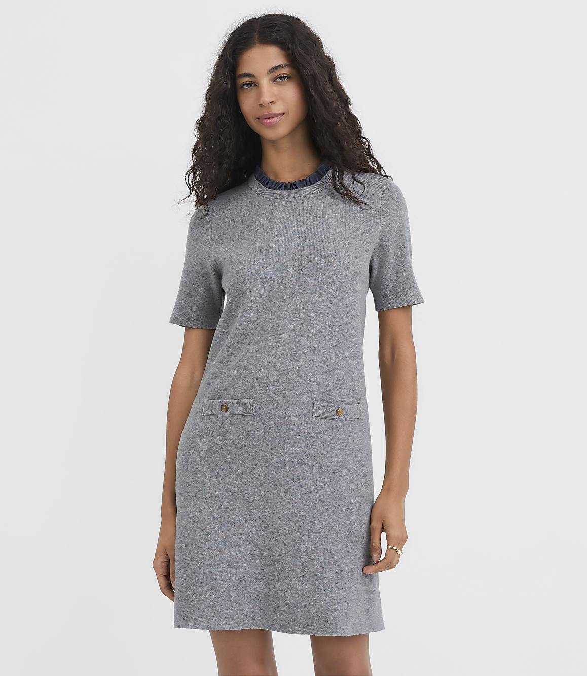 A woman in a gray knit dress with two front pockets stands against a plain white background.