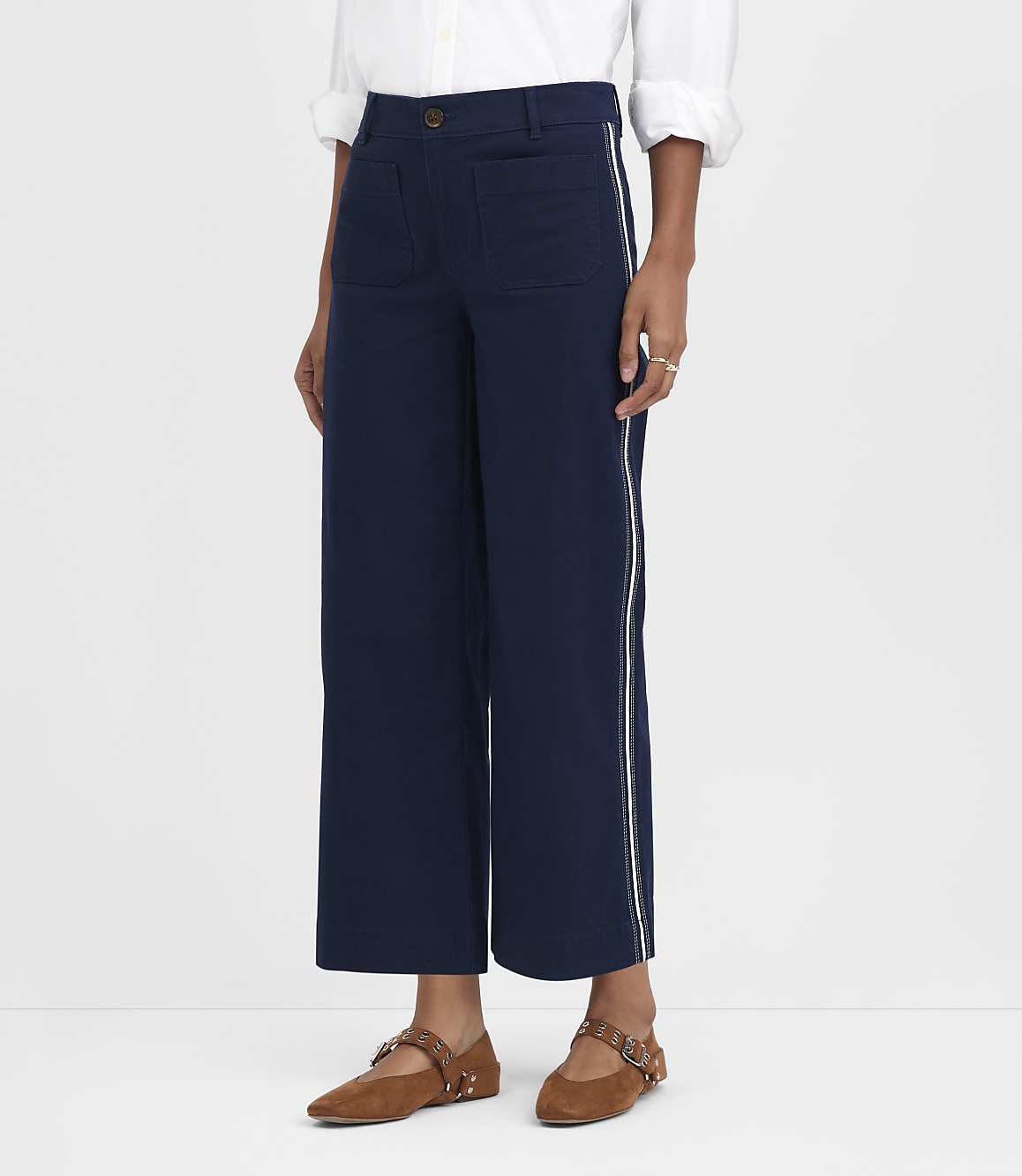 A person in navy wide-leg pants with white piping and brown flats stands against a plain white background.