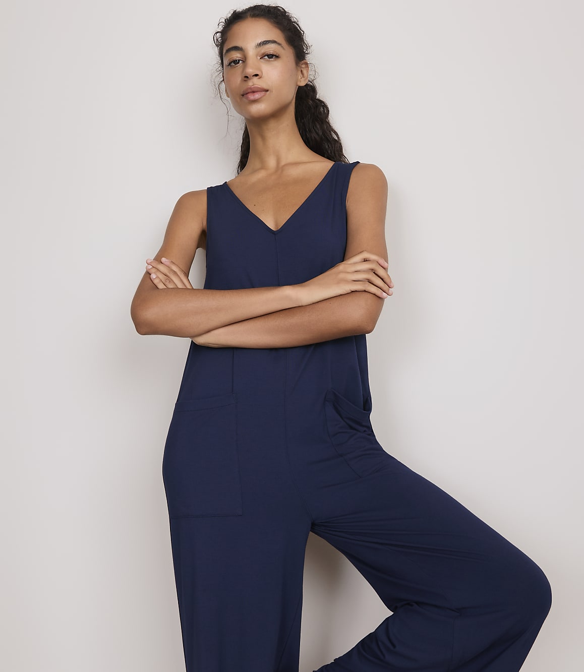 A woman in a navy blue jumpsuit stands with her arms crossed against a plain, light-colored background.