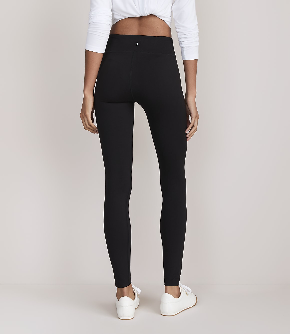 A person wearing black leggings and white sneakers stands against a plain white background.