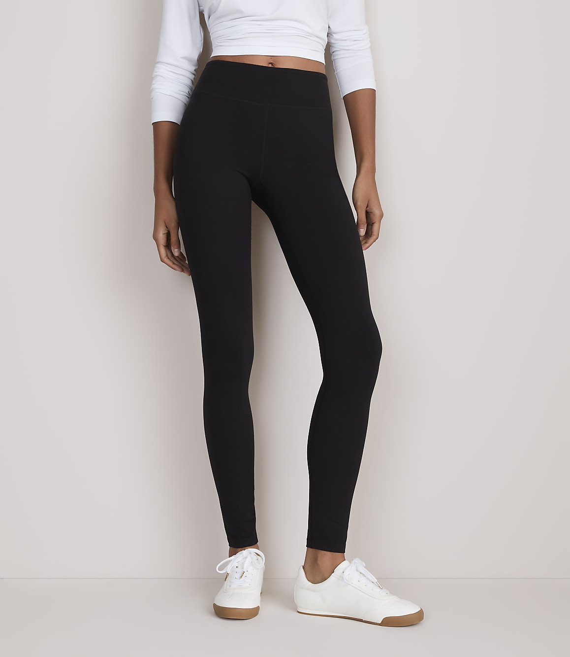 A person wearing black leggings and white sneakers stands against a plain, light-colored background.