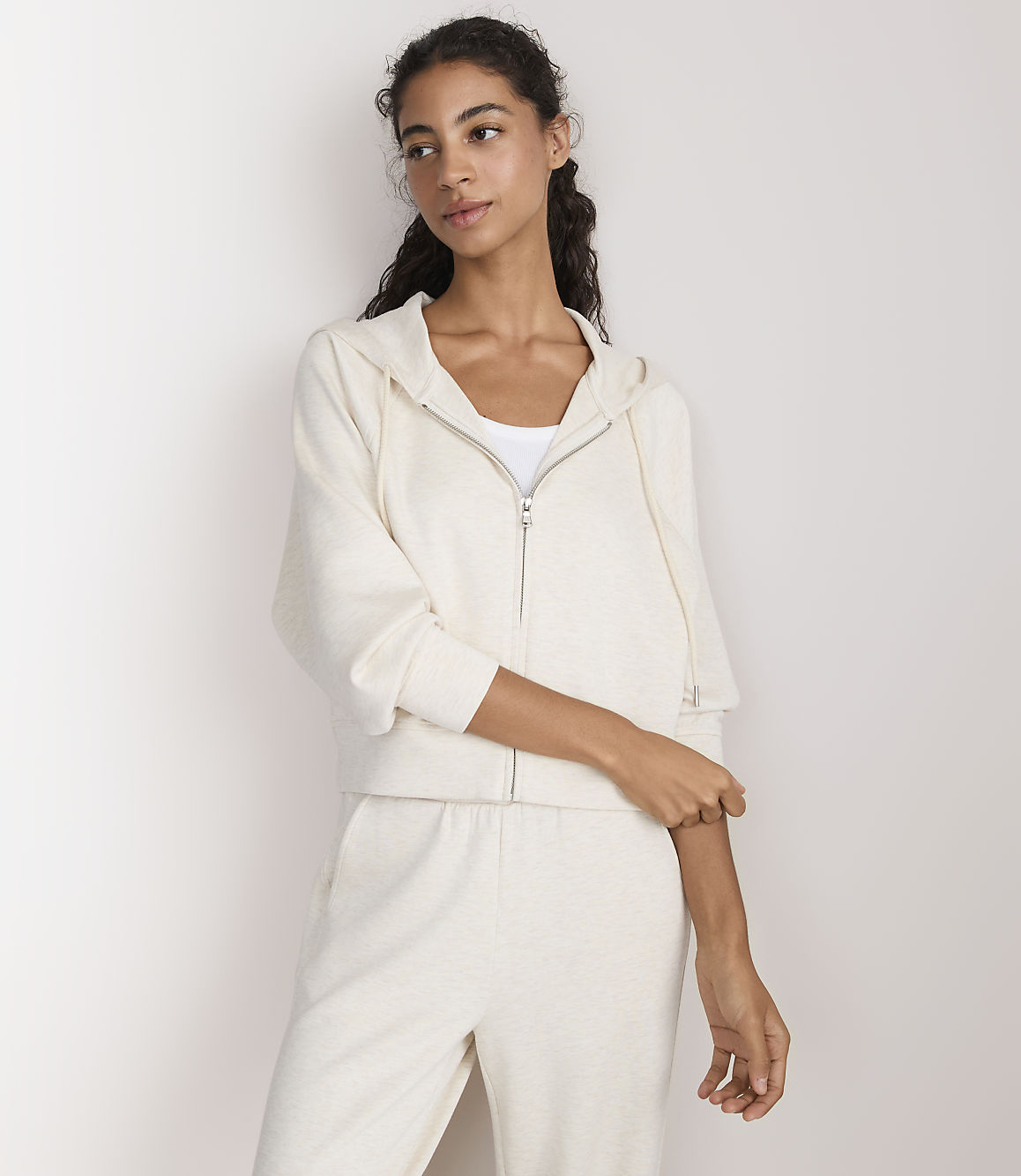 A woman in a cream-colored loungewear set stands against a plain white background.