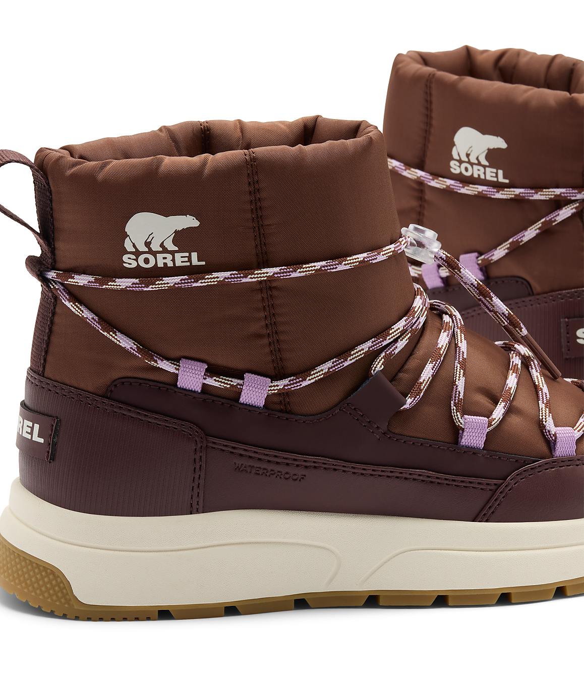 A pair of brown Sorel winter boots with white soles and purple accents are in the foreground, set against a plain white background.