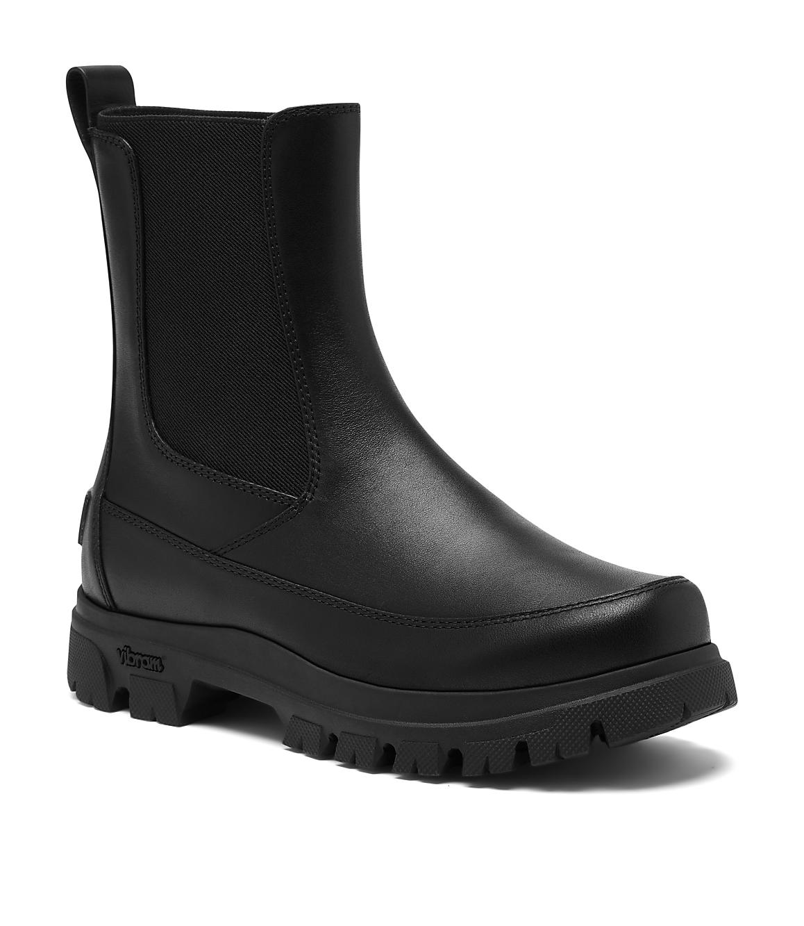 A black leather Chelsea boot with a thick lug sole stands against a plain white background.