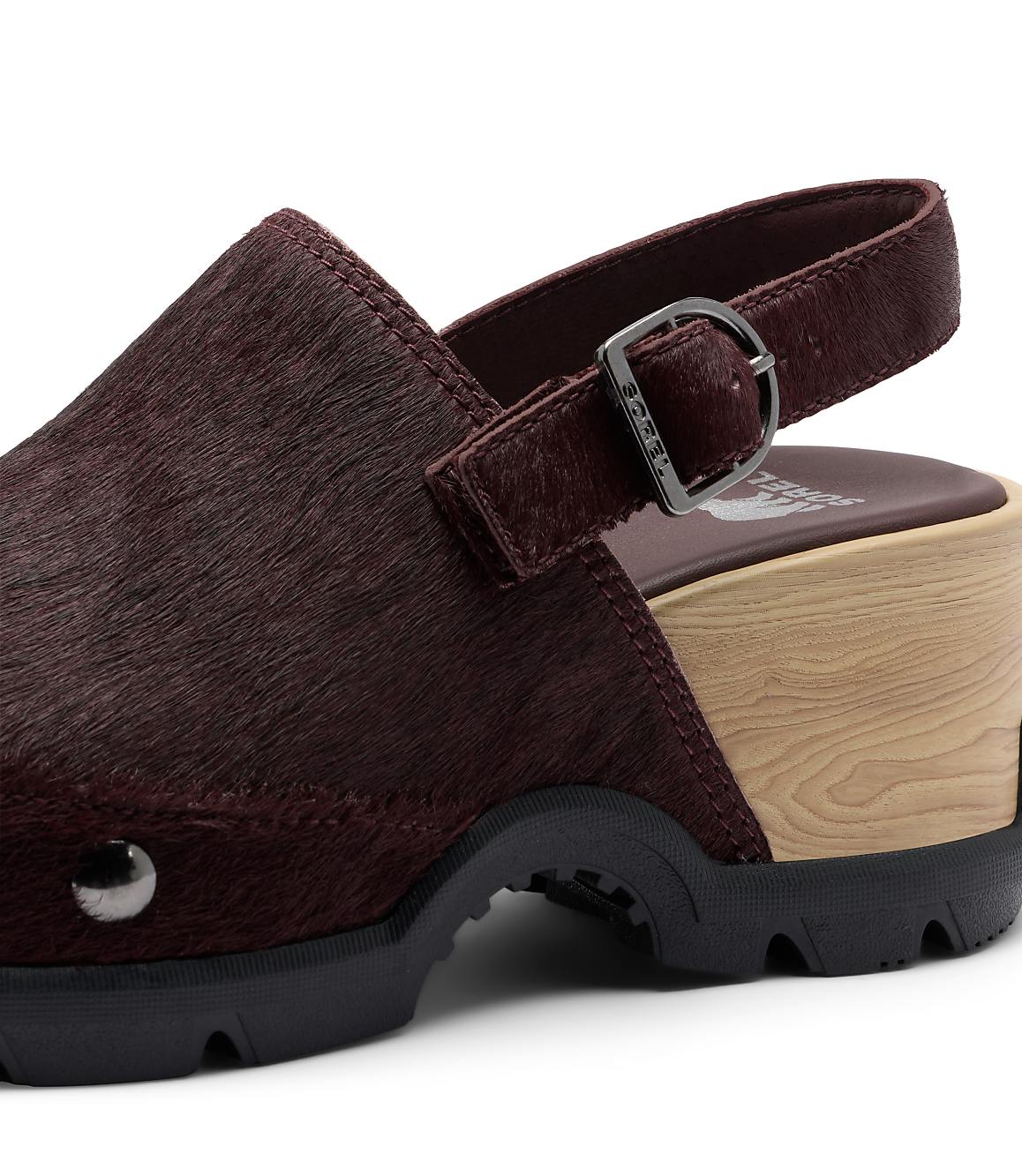 A close-up of a burgundy, furry clog with a wooden sole and a black rubber sole is set against a plain white background.