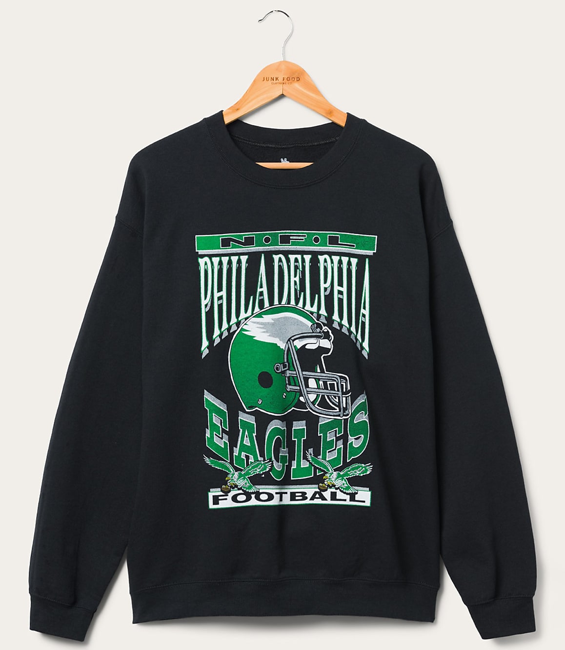 A black Philadelphia Eagles sweatshirt with a graphic of a helmet and eagles hangs on a wooden hanger against a plain white background.
