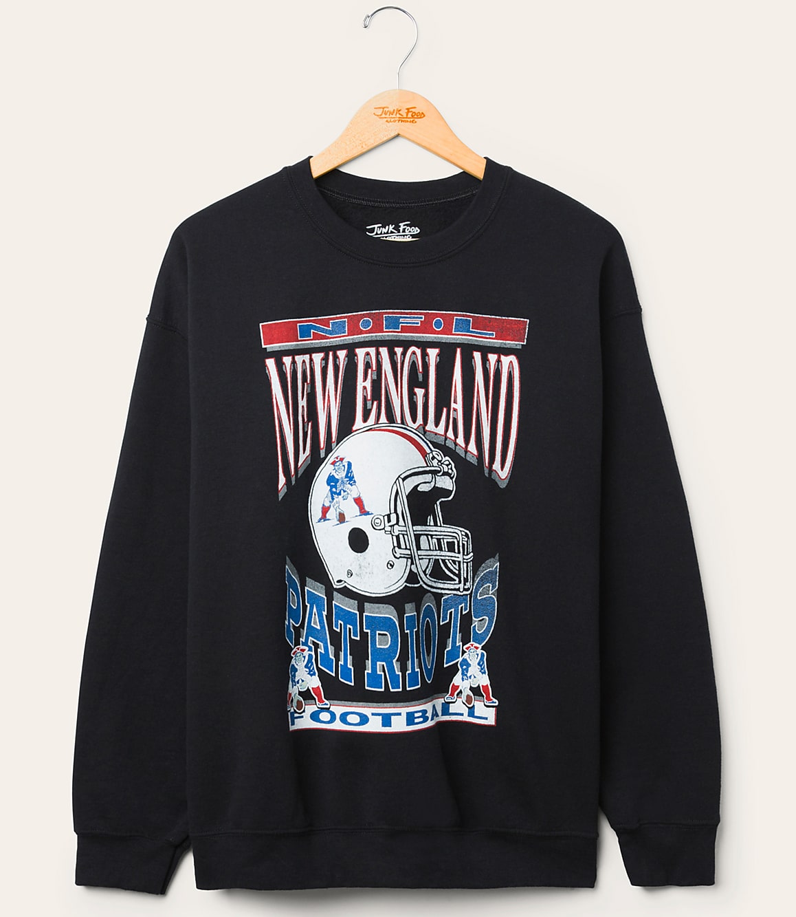A black New England Patriots sweatshirt with a graphic of a helmet and team name hangs on a wooden hanger against a plain, light-colored background.