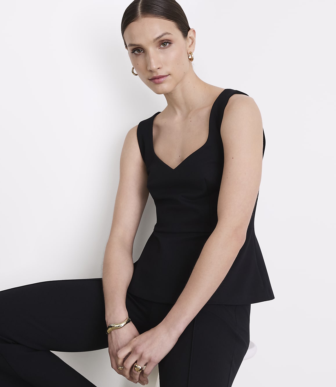 A woman in a black peplum top and pants poses against a plain white background.