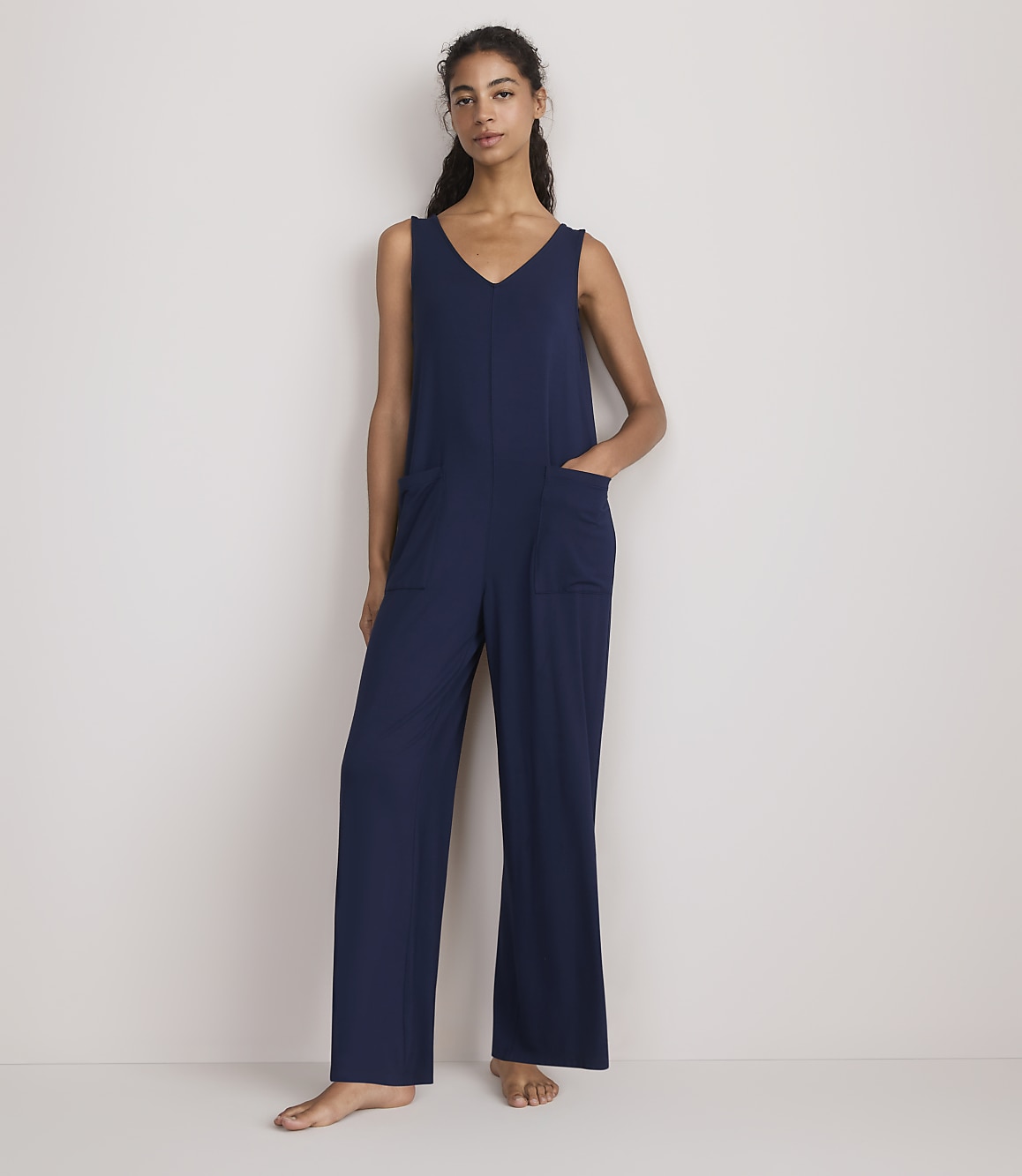 A woman in a navy blue jumpsuit stands against a plain white background.