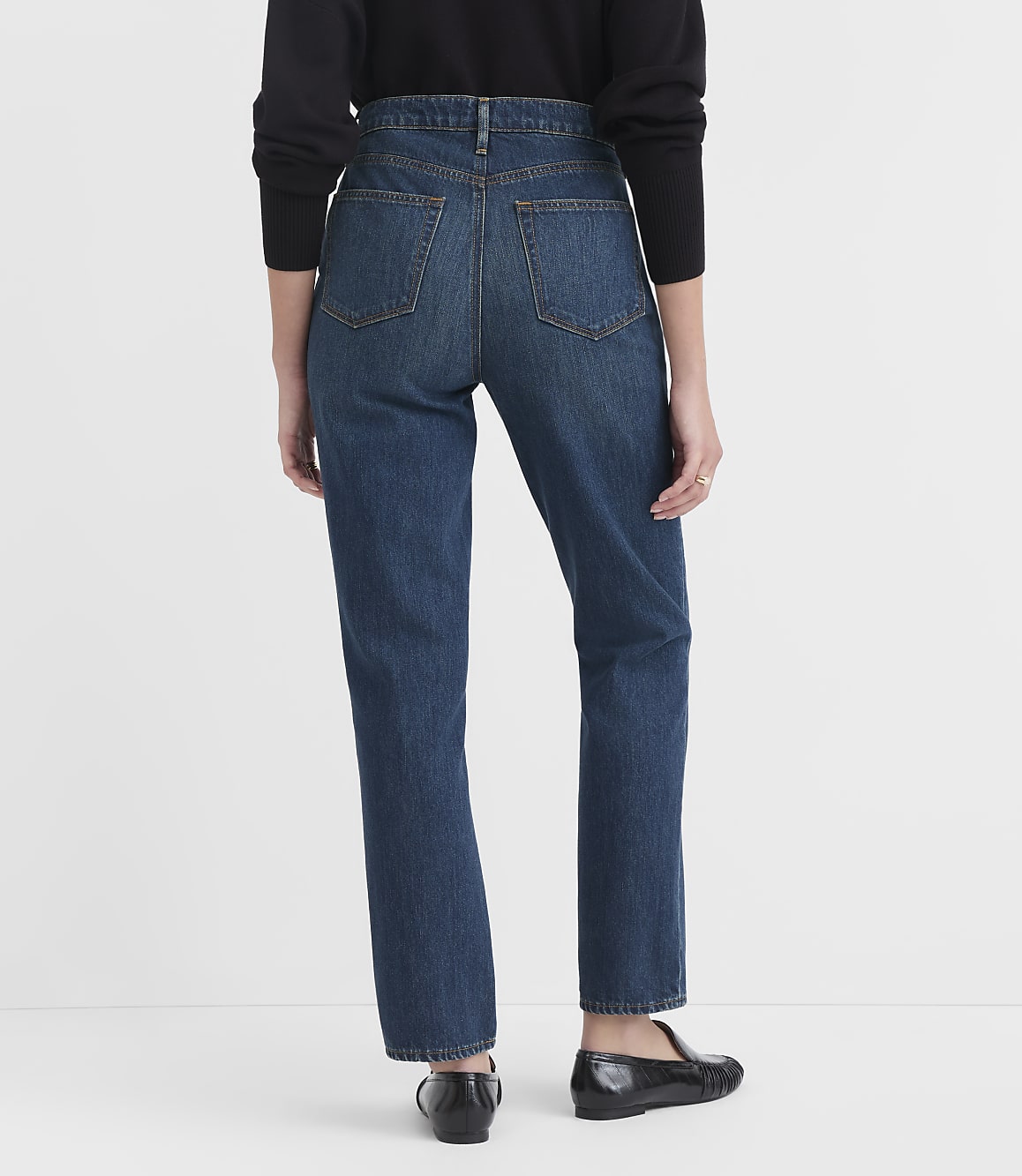 A person wearing dark wash jeans and black loafers stands against a plain white background.
