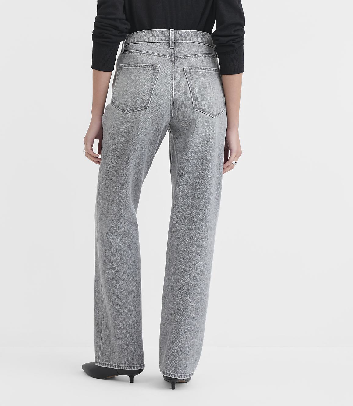 A person wearing grey wide-leg jeans and black shoes stands against a plain white background.