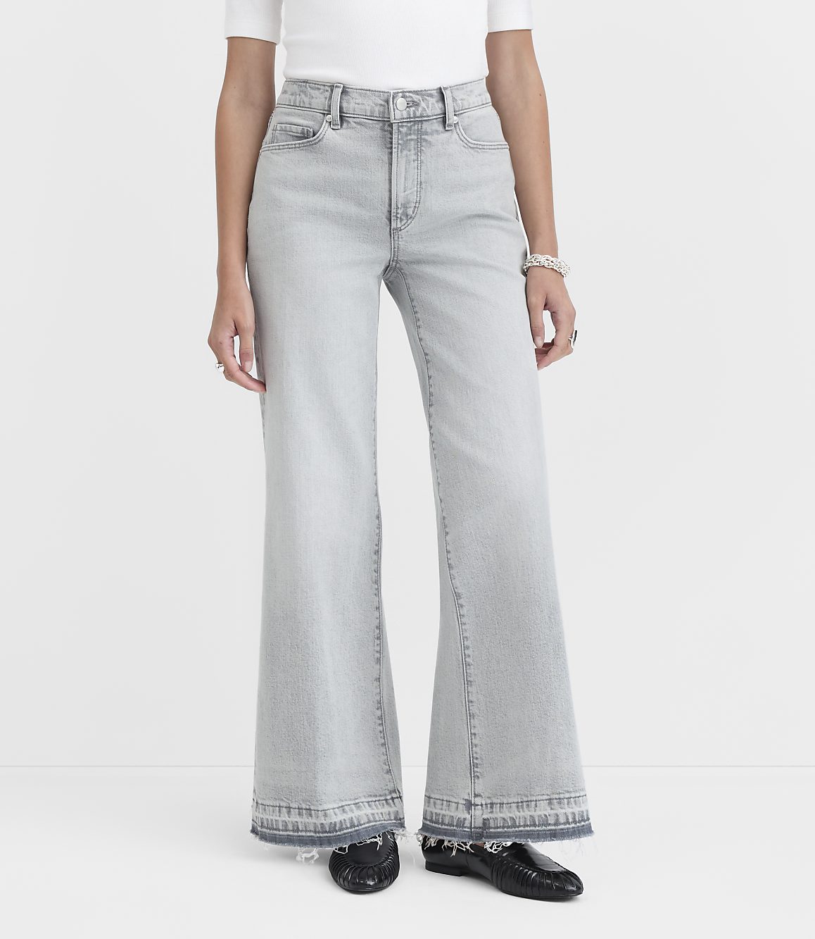A person stands in light-wash flared jeans with frayed hems and black loafers against a plain white background.