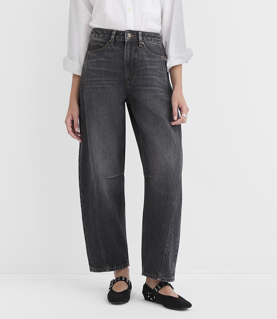 A person wearing dark wash, wide-leg jeans and black studded flats stands against a plain white background.