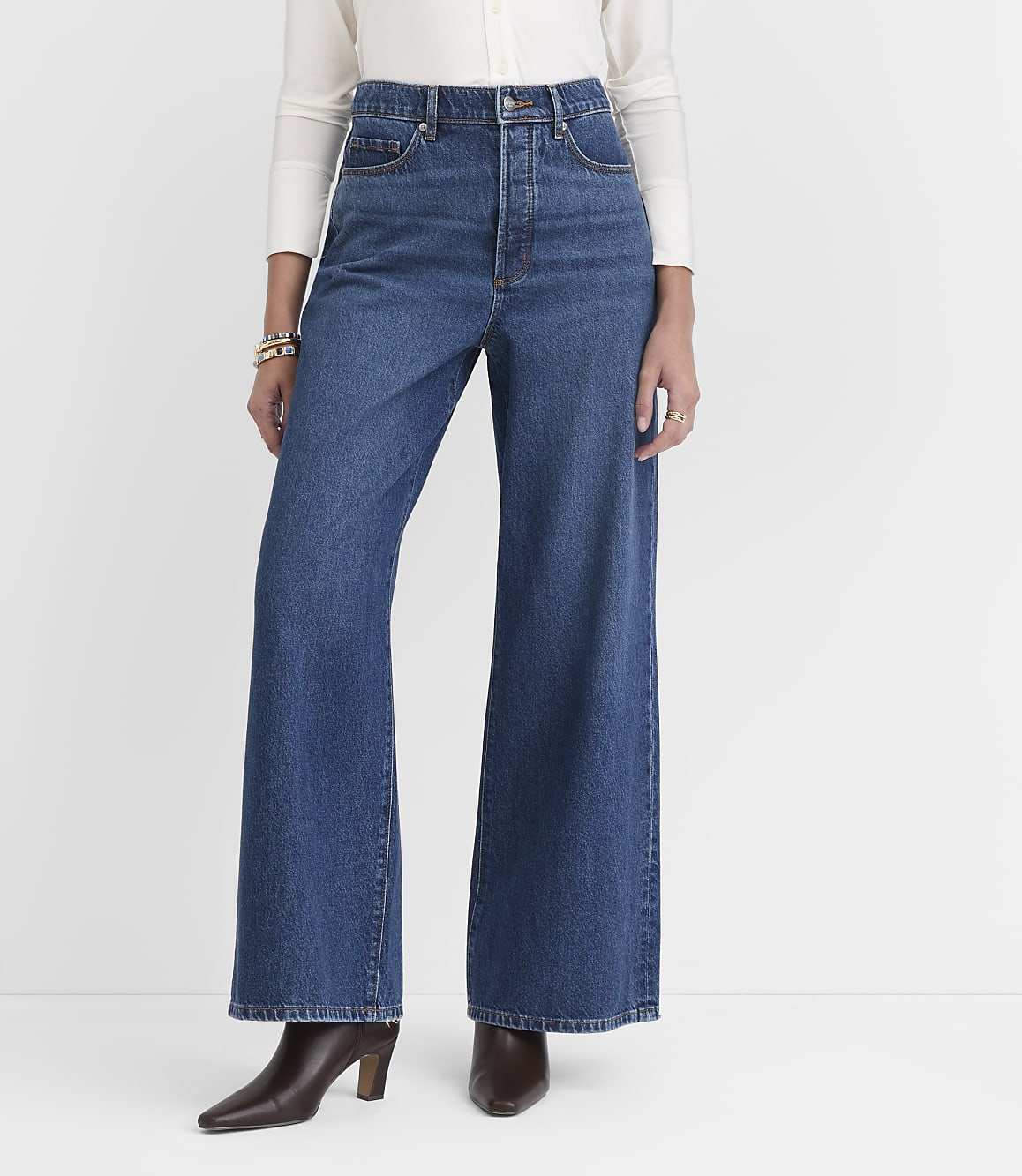 A person stands in wide-leg blue jeans and brown heeled boots against a plain white background.