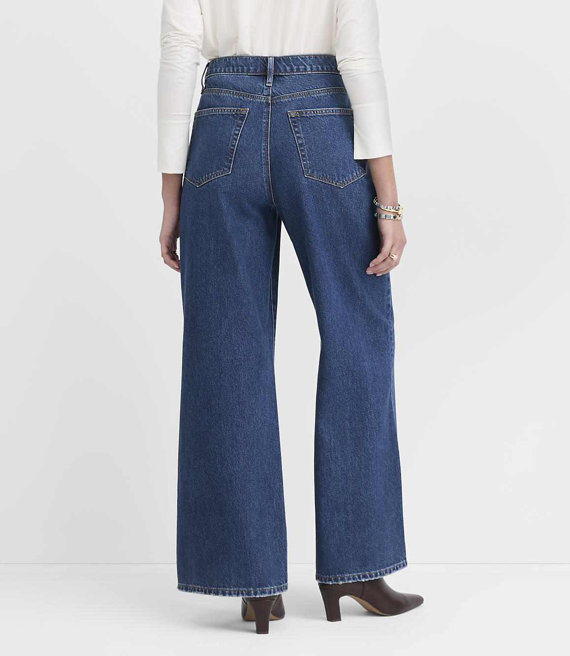 A person wearing wide-leg blue jeans and a white top stands against a plain white background.