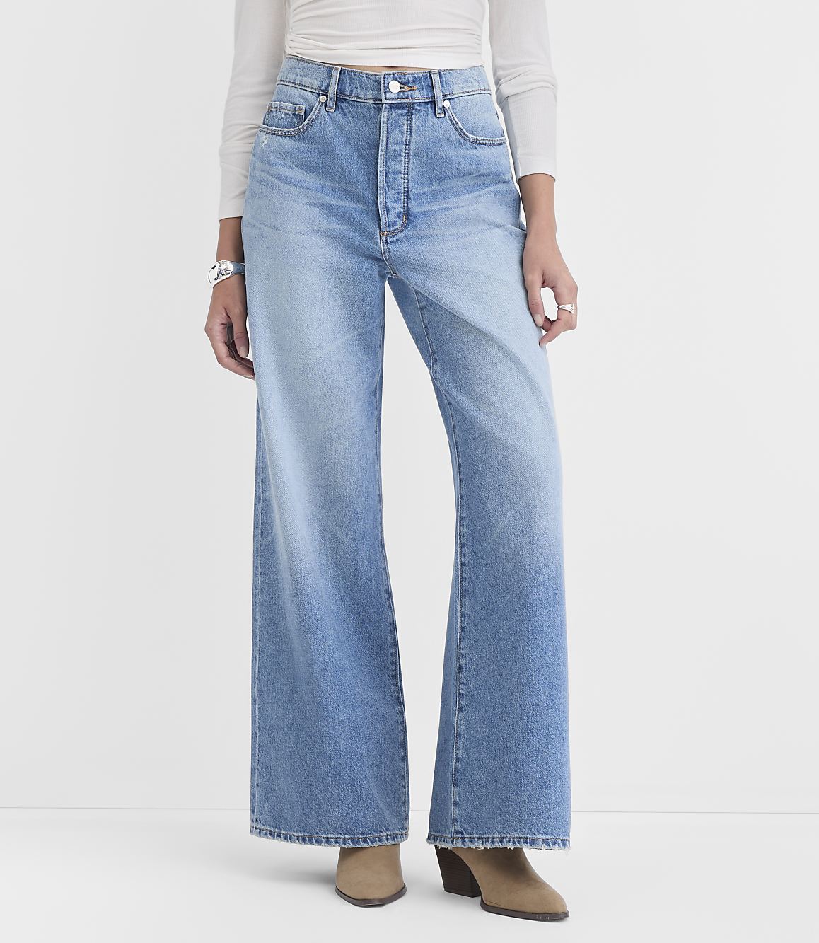 A person in light blue wide-leg jeans and a white top stands against a plain white background.