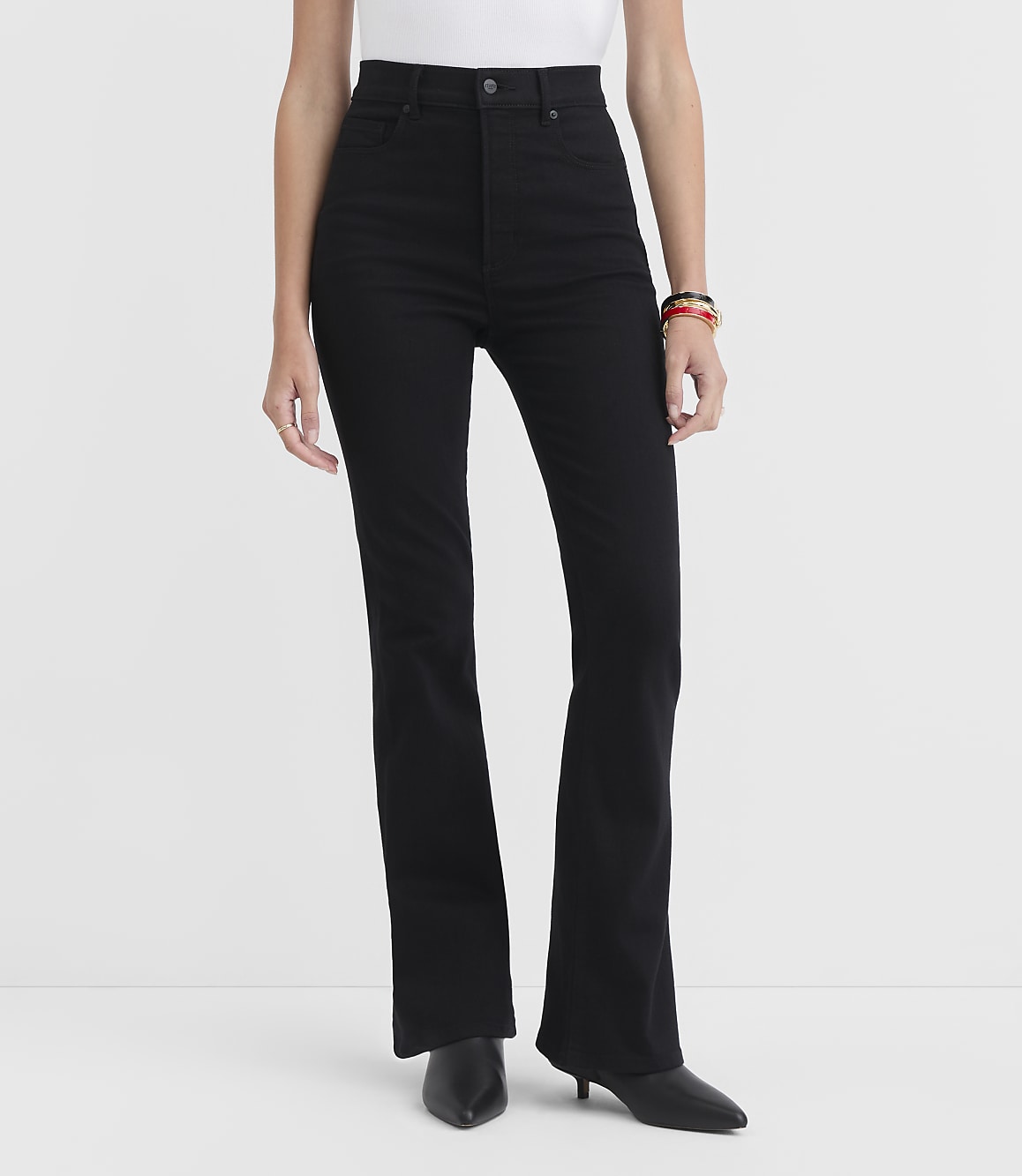 A person wearing black flare jeans and black heeled boots stands against a plain white background.