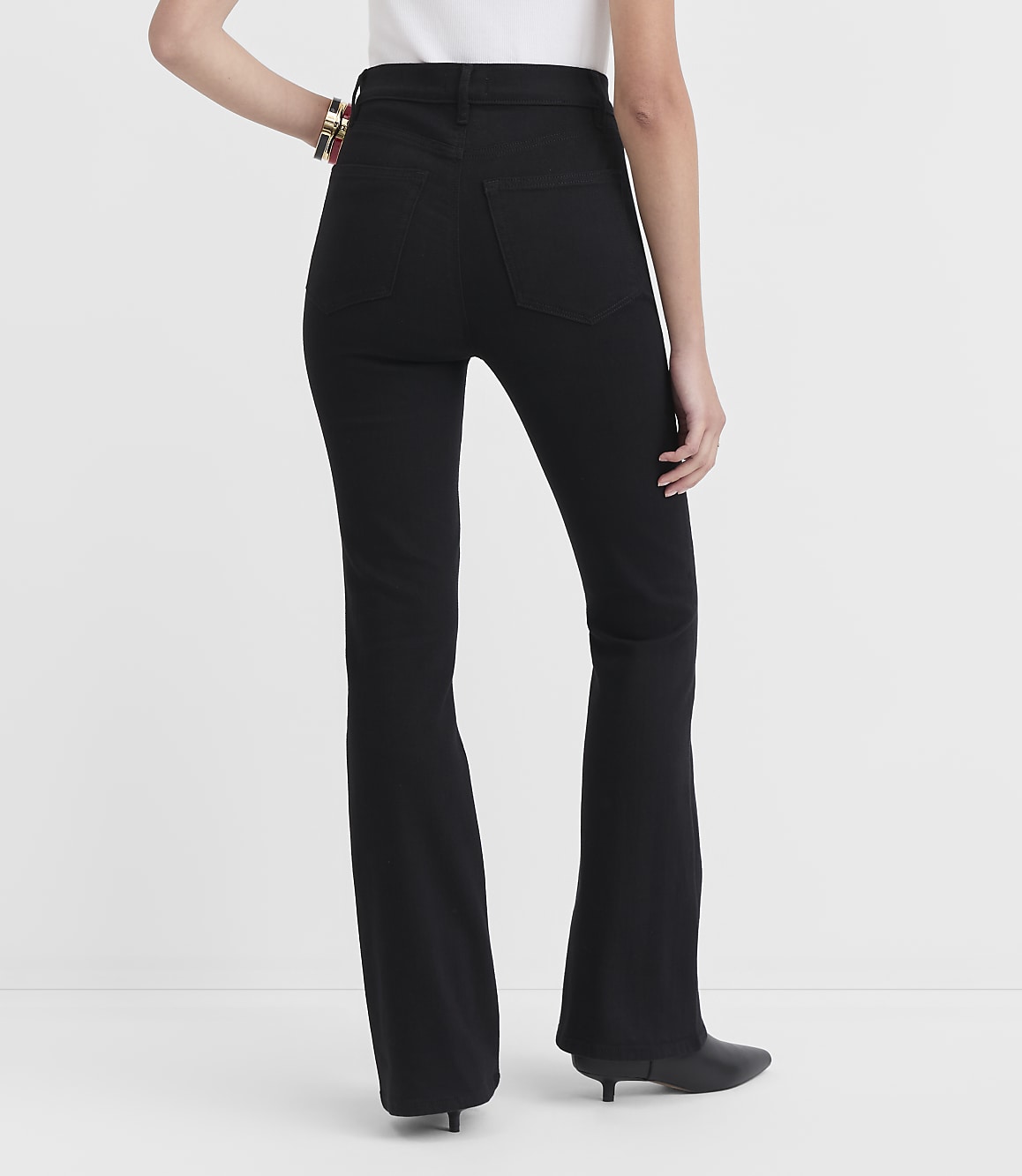A person wearing black flare jeans and black heeled boots stands against a plain white background.