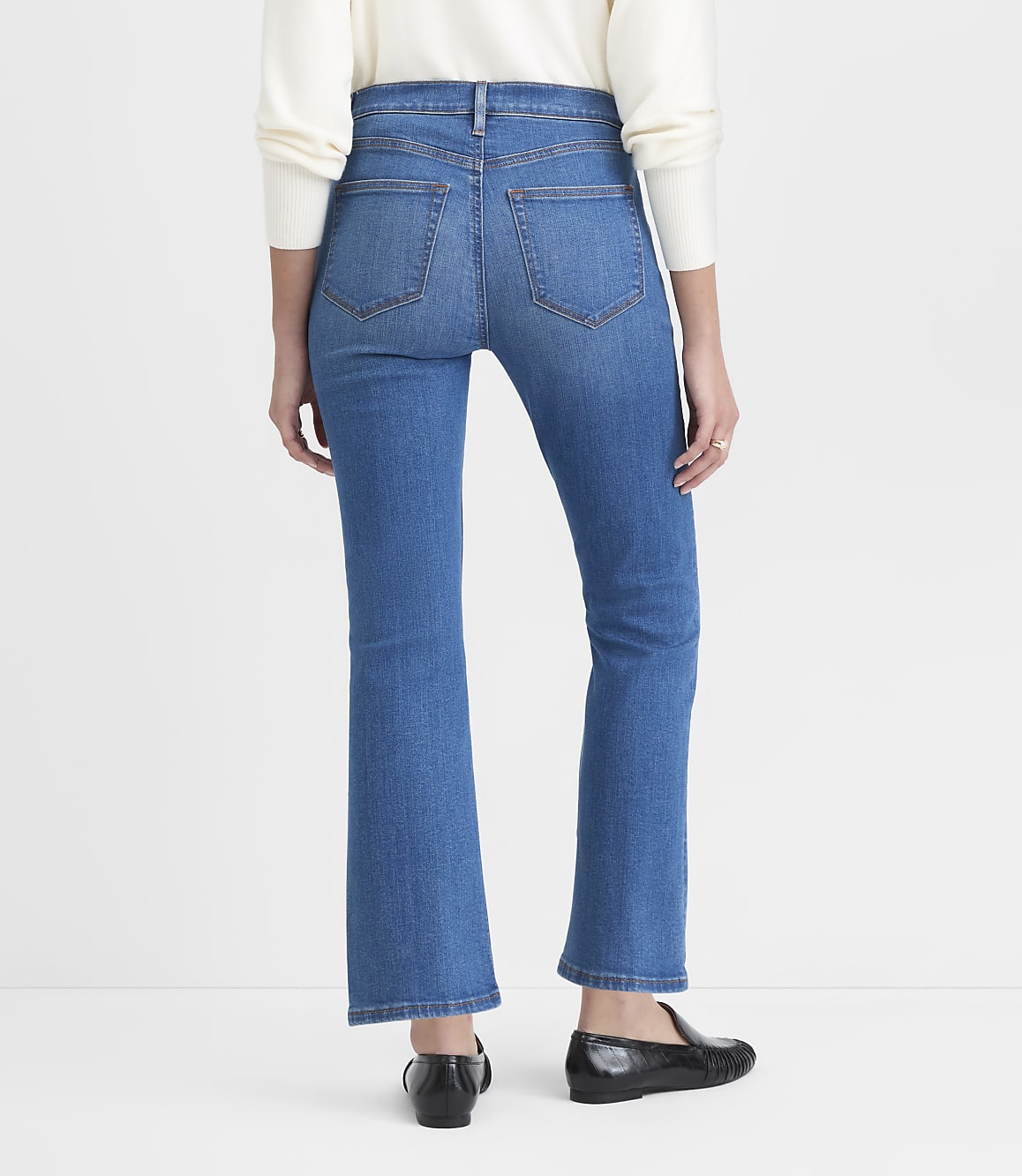 A person wearing flared blue jeans and black shoes stands against a plain white background.