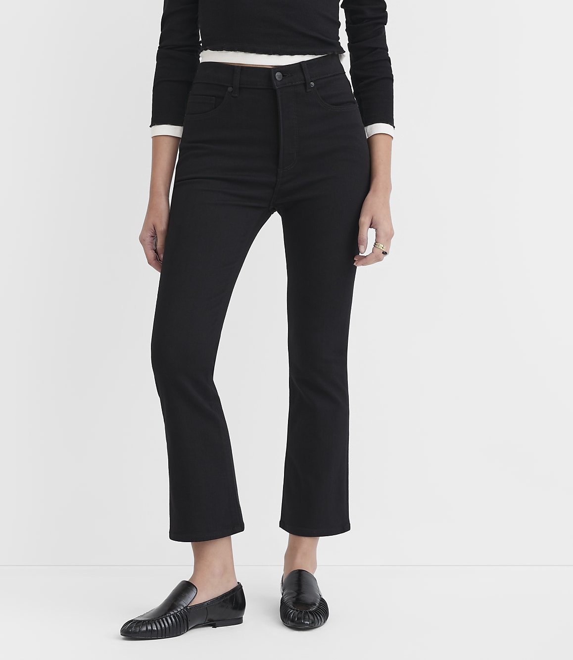 A person wearing black jeans and loafers stands against a plain white background.