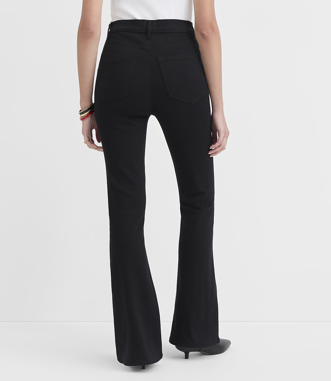 A person wearing black flare jeans stands against a plain white background.