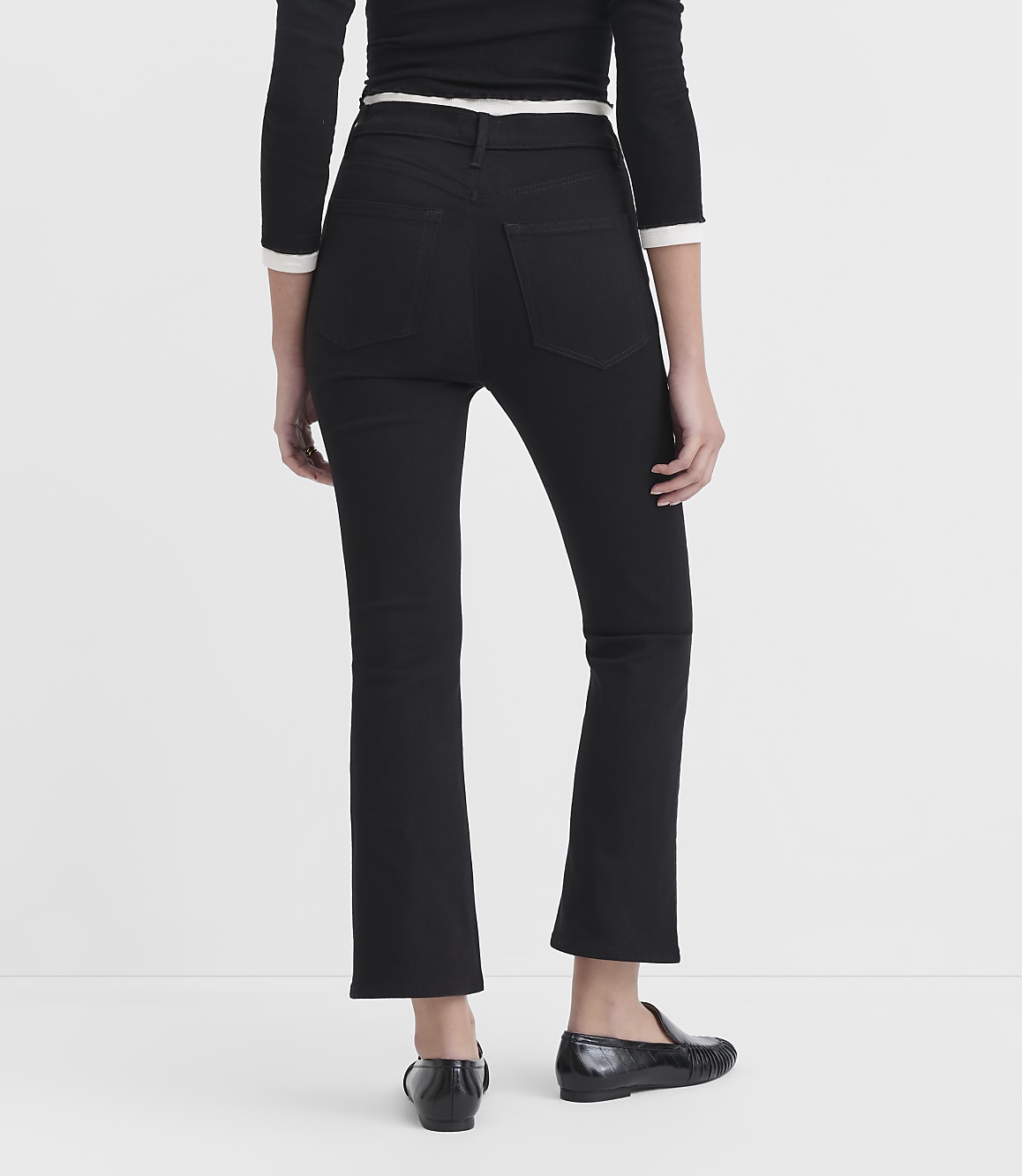A person wearing black flared jeans and black loafers stands against a plain white background.