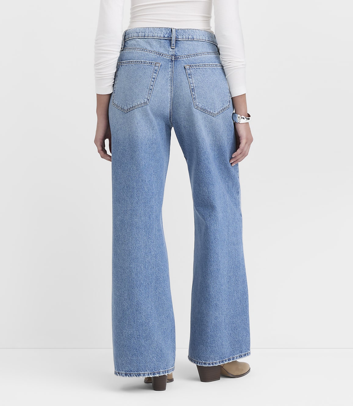 A person wearing light blue wide-leg jeans and a white long-sleeved shirt stands against a plain white background.