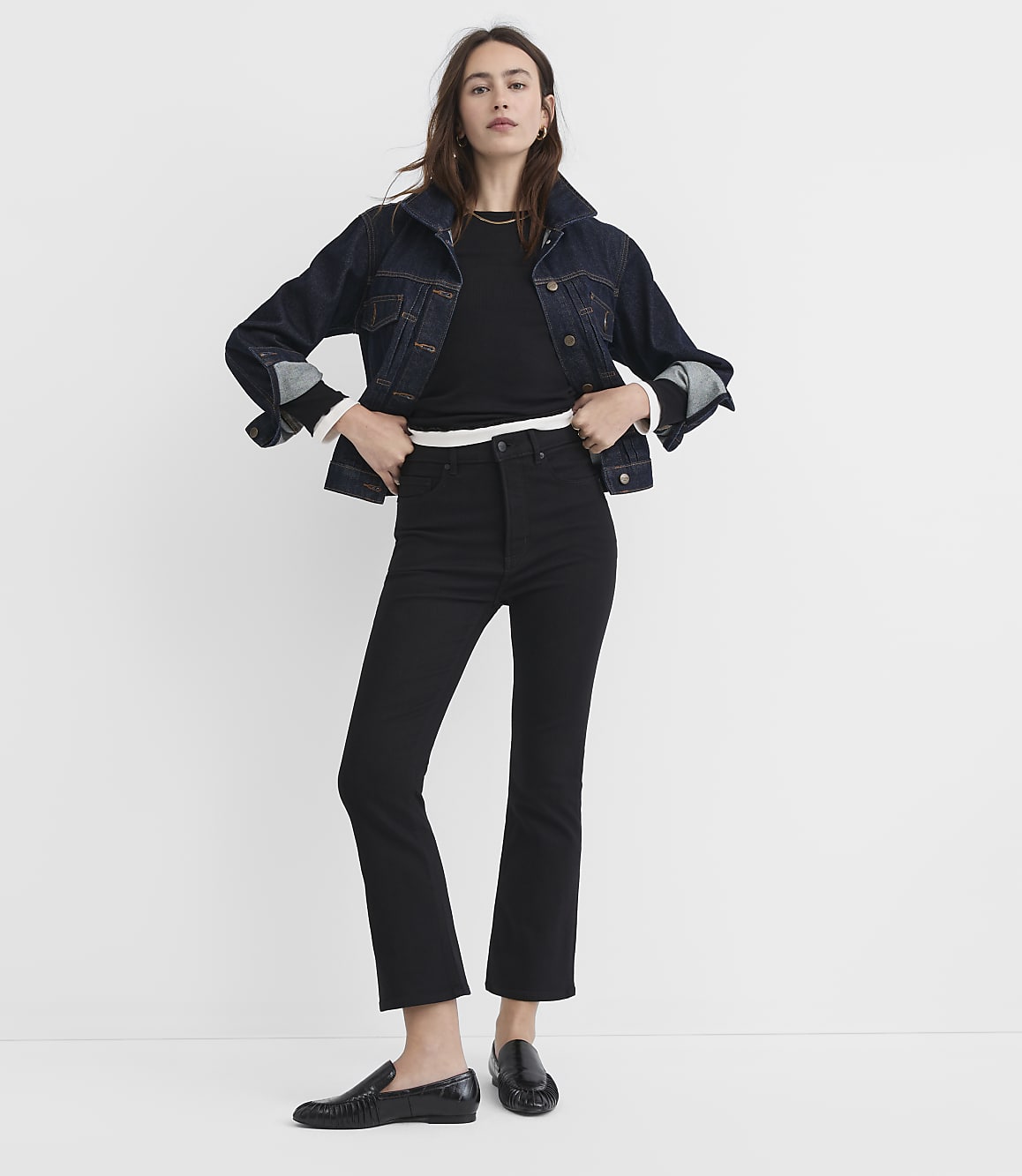 A woman in a denim jacket and black jeans stands against a plain white background.