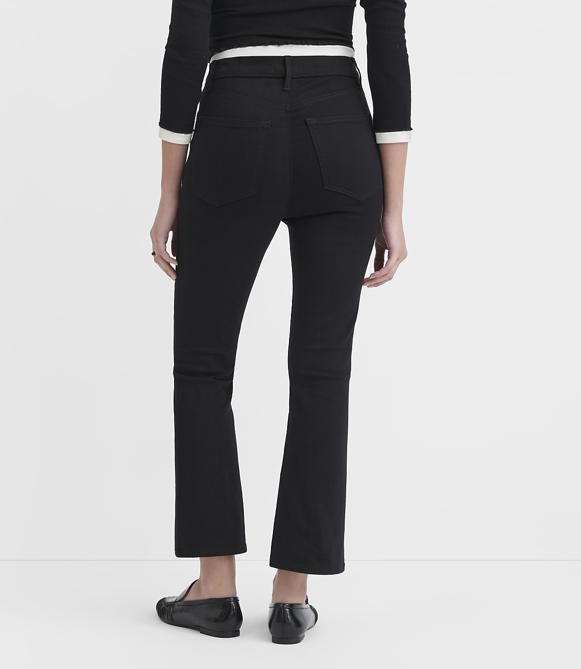 A person wearing black flared jeans and black loafers stands against a plain white background.