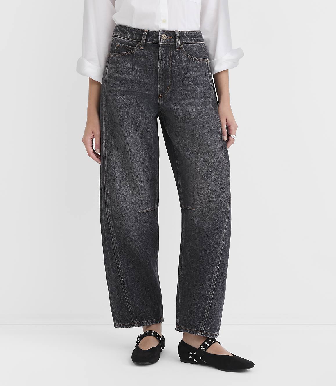 A person stands in the foreground wearing dark wash, wide-leg jeans and black flats, against a plain white background.