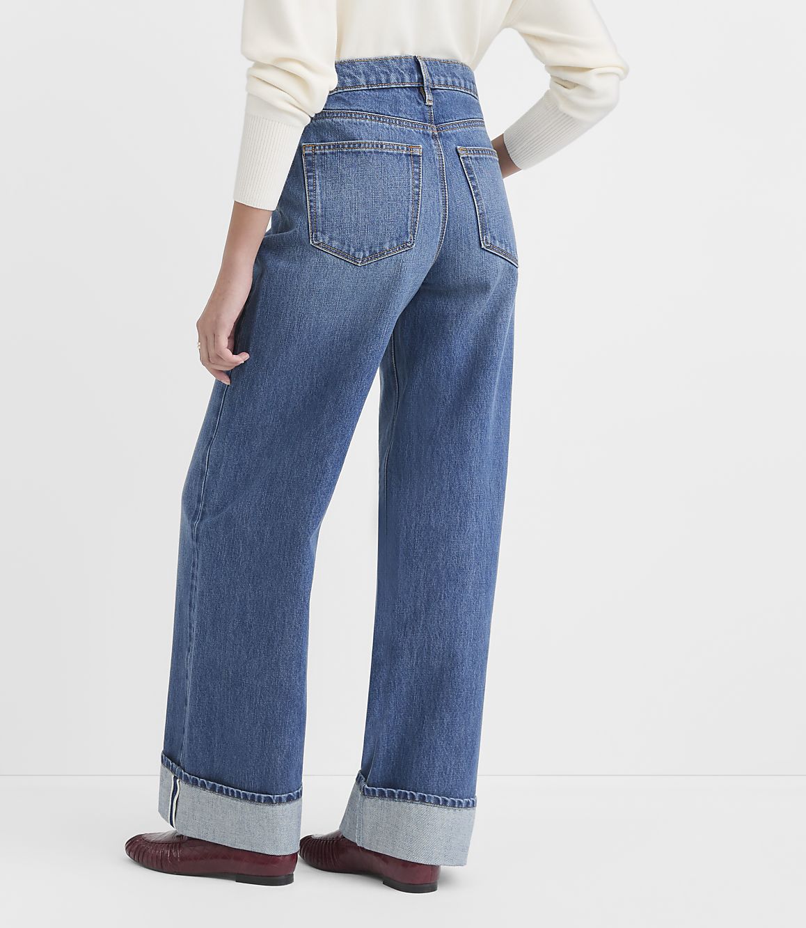 A person wearing cuffed wide-leg jeans and loafers stands against a plain white background.