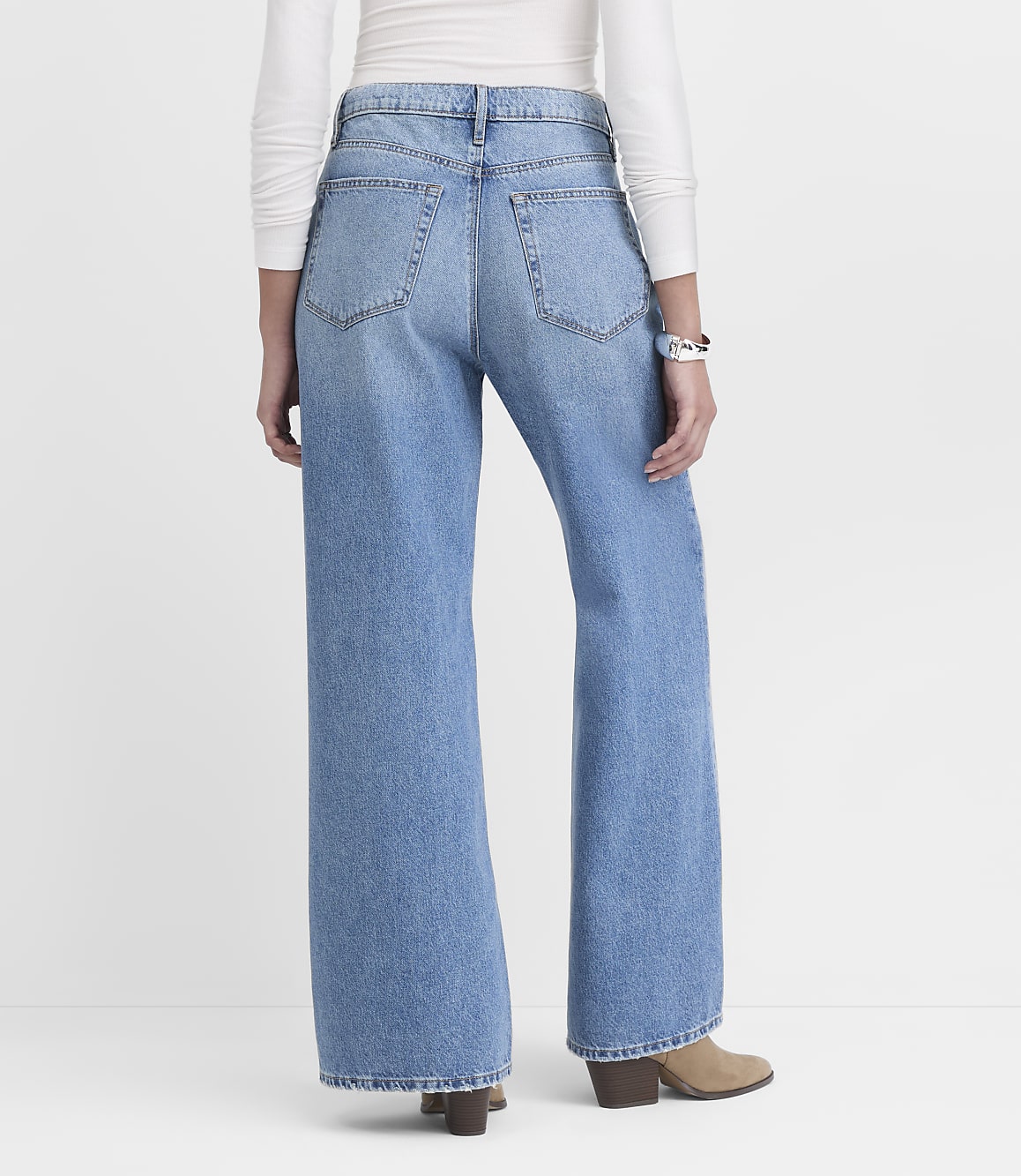 A person wearing light-wash wide-leg jeans and tan boots stands against a plain white background.