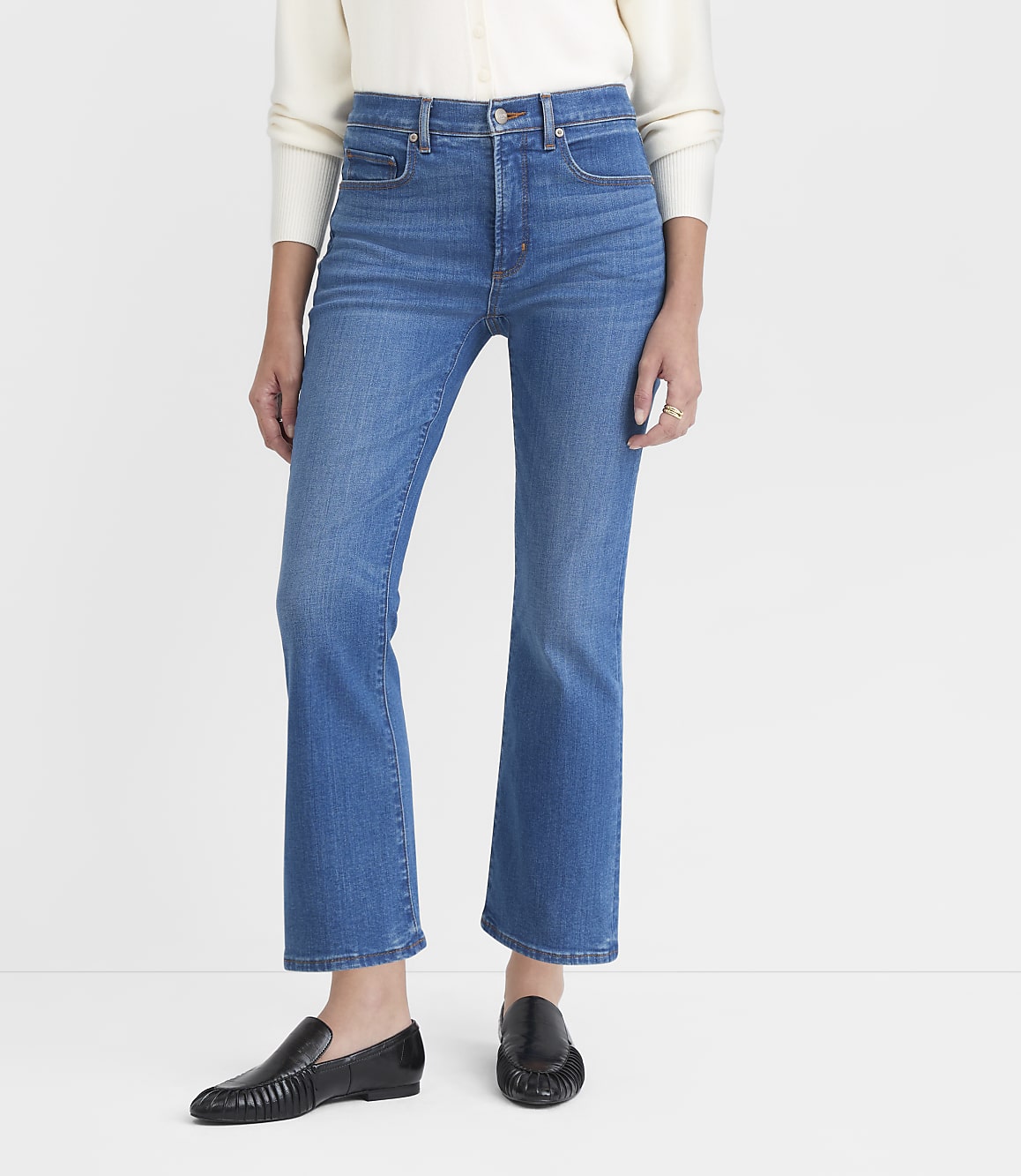 A person wearing blue jeans and black loafers stands against a plain white background.