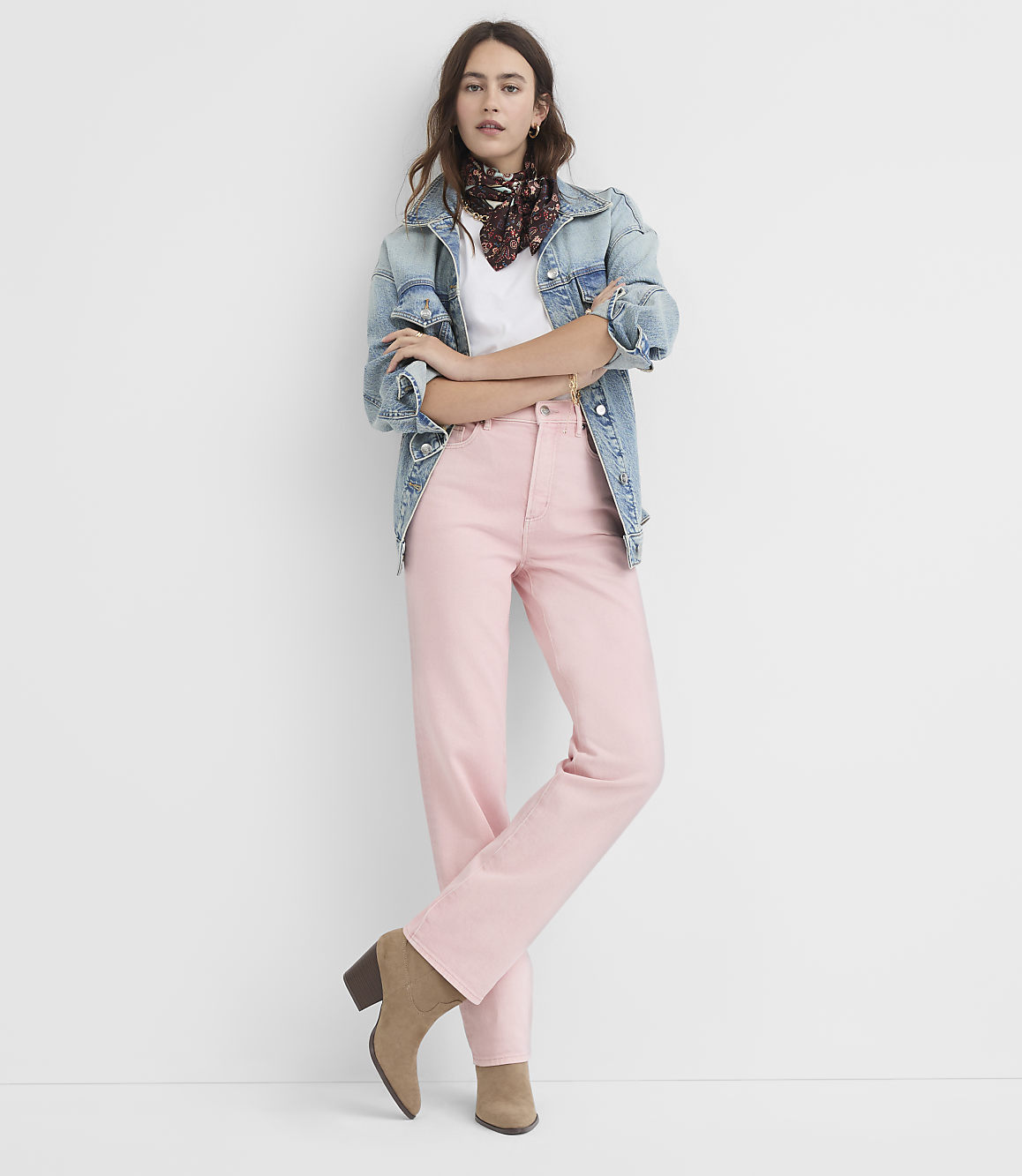 A woman in a denim jacket and pink pants stands against a plain white background.