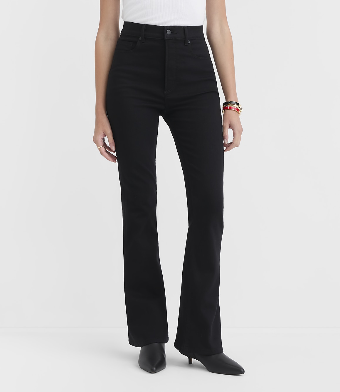 A person stands in black flare jeans and black heels against a plain white background.
