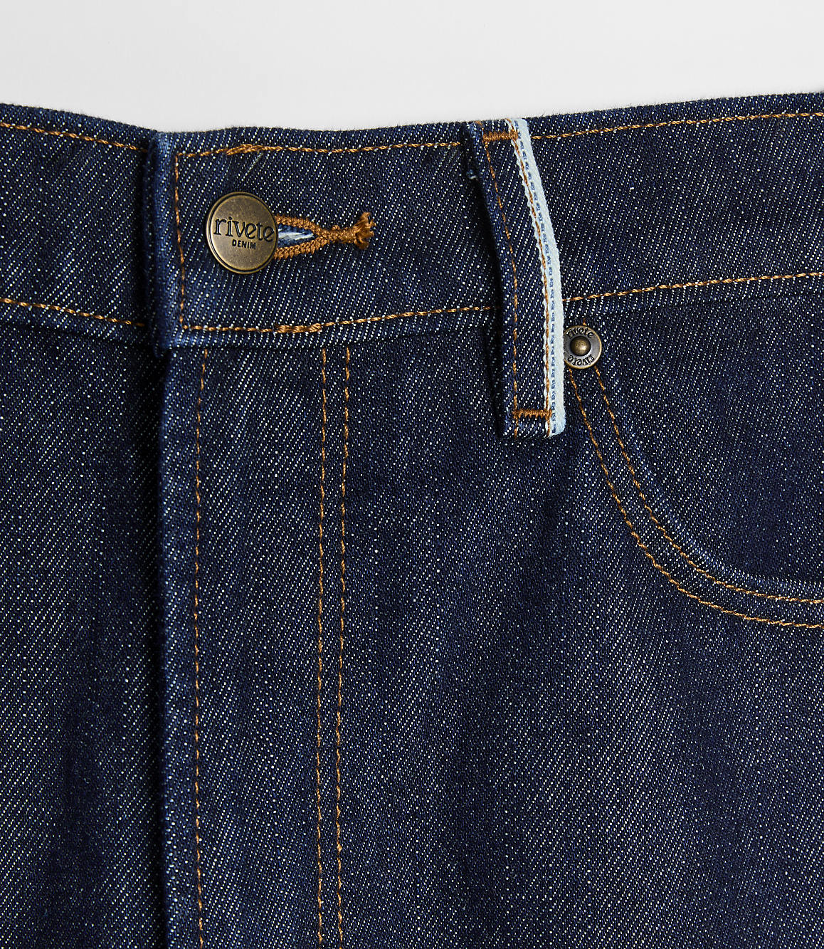 Dark wash denim jeans with copper button and stitching in the foreground are set against a plain white background.