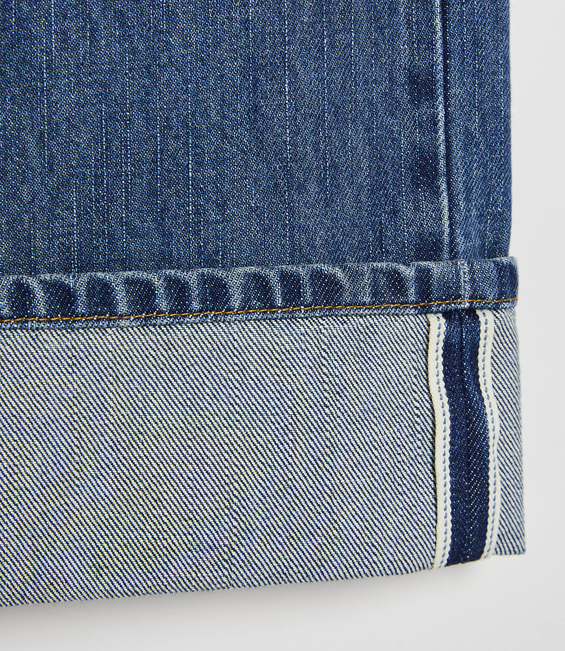 A close-up of cuffed blue denim jeans with a white background.