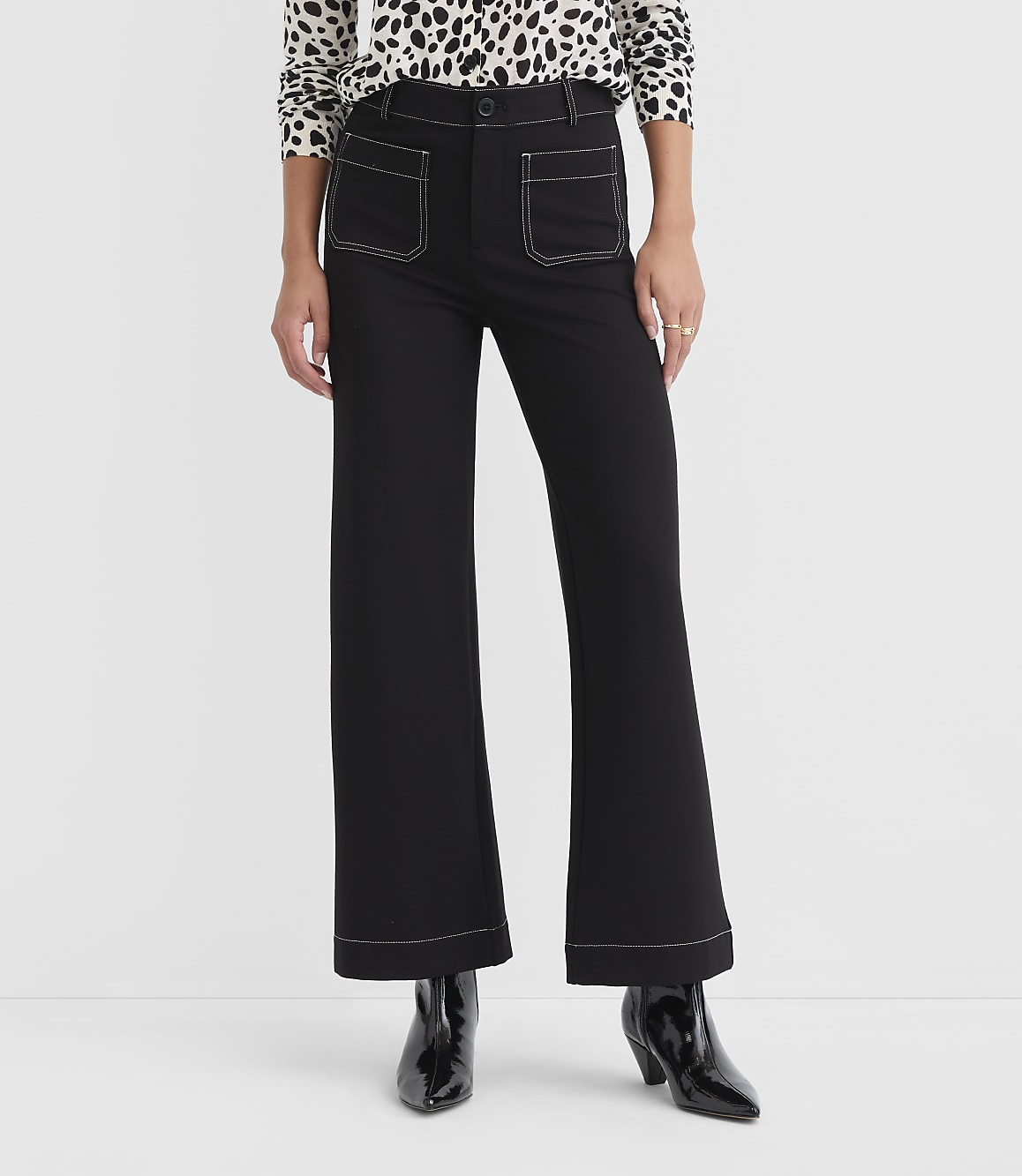 A person stands in black flared pants with white stitching and a leopard print top, against a plain white background.