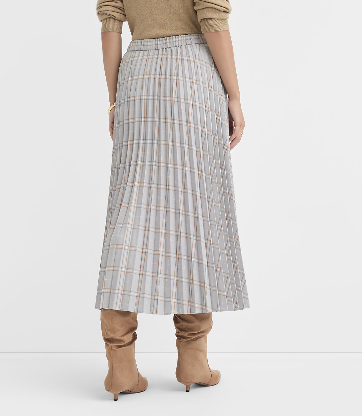 A person wearing a plaid pleated skirt and brown boots stands against a plain white background.