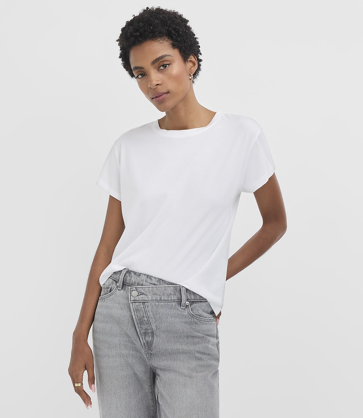 A woman in a white t-shirt and grey jeans stands against a plain white background.