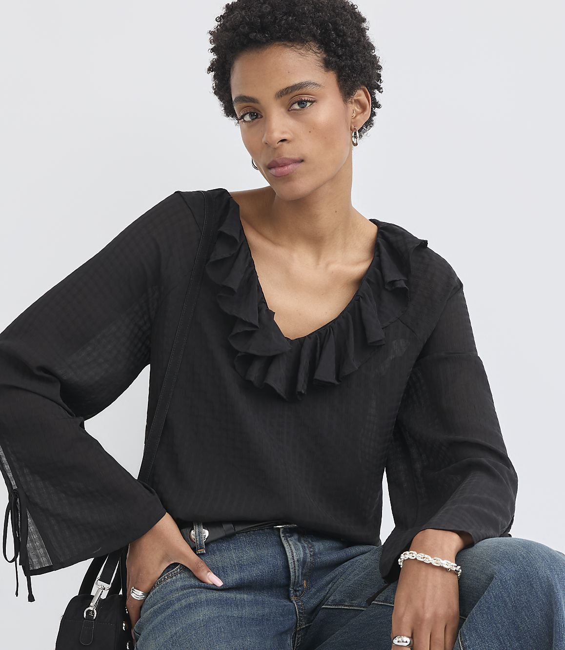 A woman with short, dark hair and a ruffled black blouse poses against a plain white background.