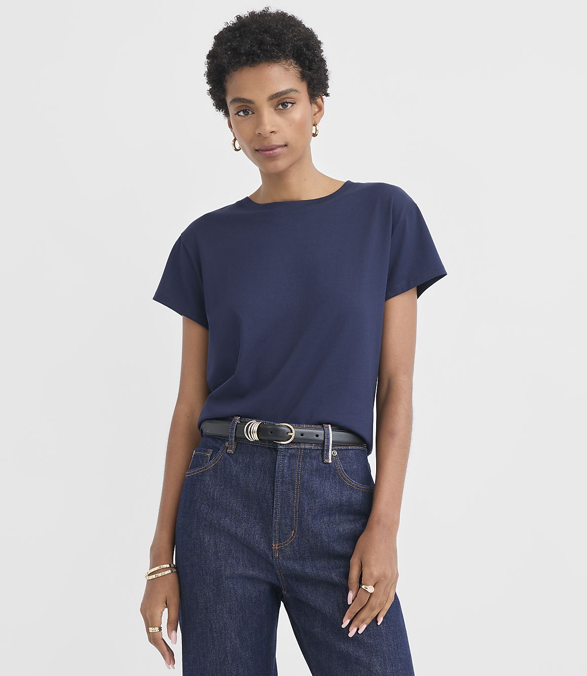A woman in a navy t-shirt and dark wash jeans stands against a plain white background.