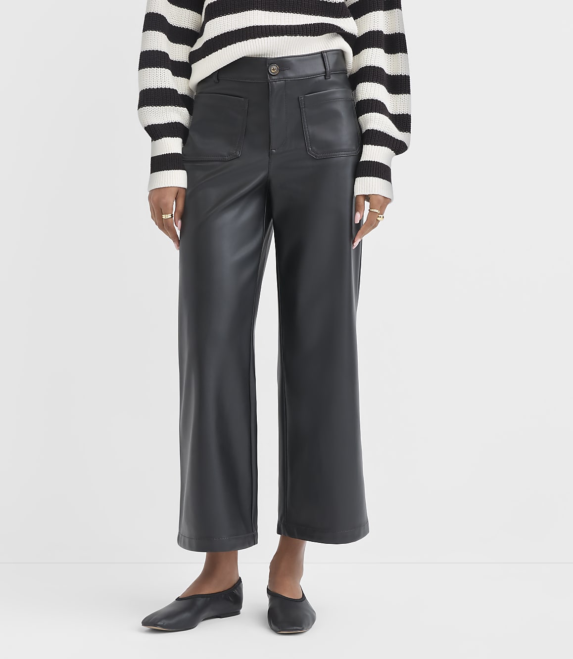 A person stands in black faux leather pants and a striped sweater, against a plain white background.